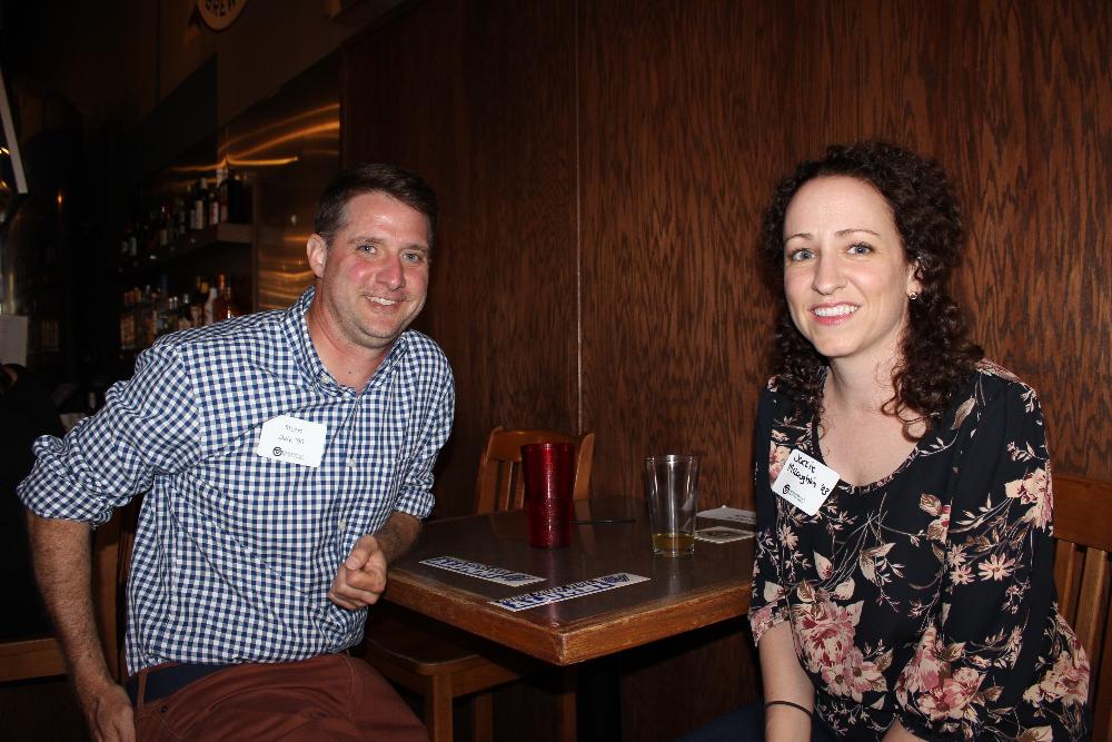 Two alumni sitting at a table smiling for camera